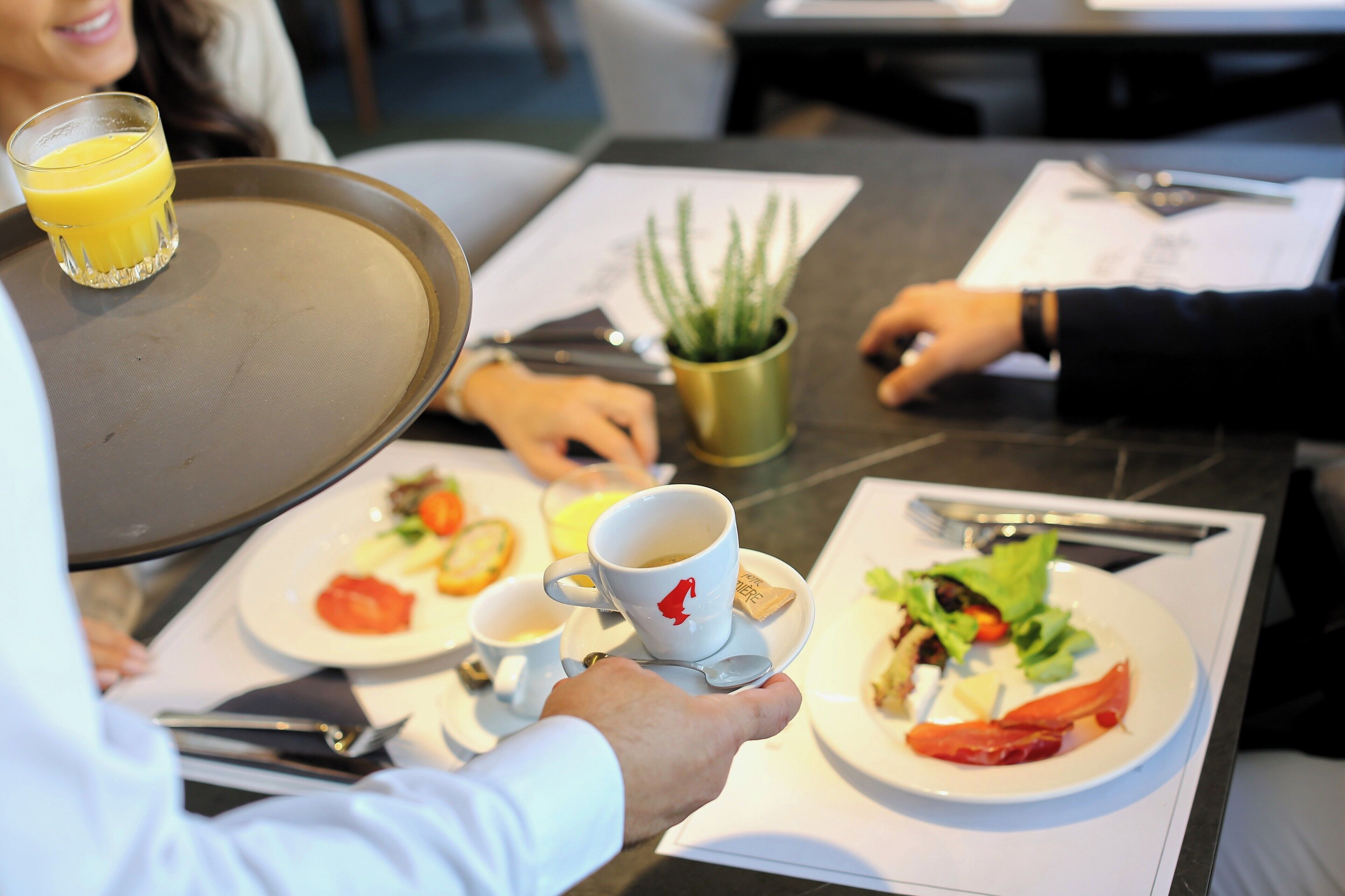 Une table à manger avec des assiettes remplies de nourriture, une tasse de café et un verre de jus d’orange.
