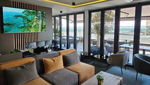 A modern hotel room with a large TV, comfortable seating, and a balcony with outdoor furniture. - Lumière Hotel (Belgrade)