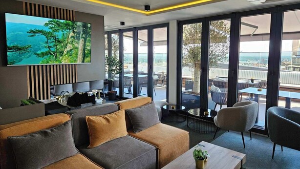A modern hotel room with a large TV, comfortable seating, and a balcony with outdoor furniture. - Lumière Hotel (Belgrade)