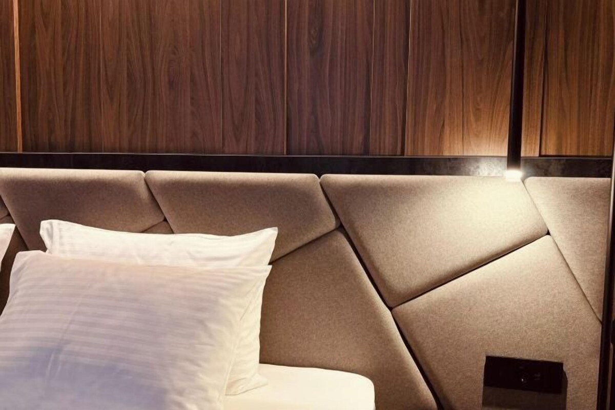 A bed with a headboard, a white pillow, and a wooden panel wall in the background.