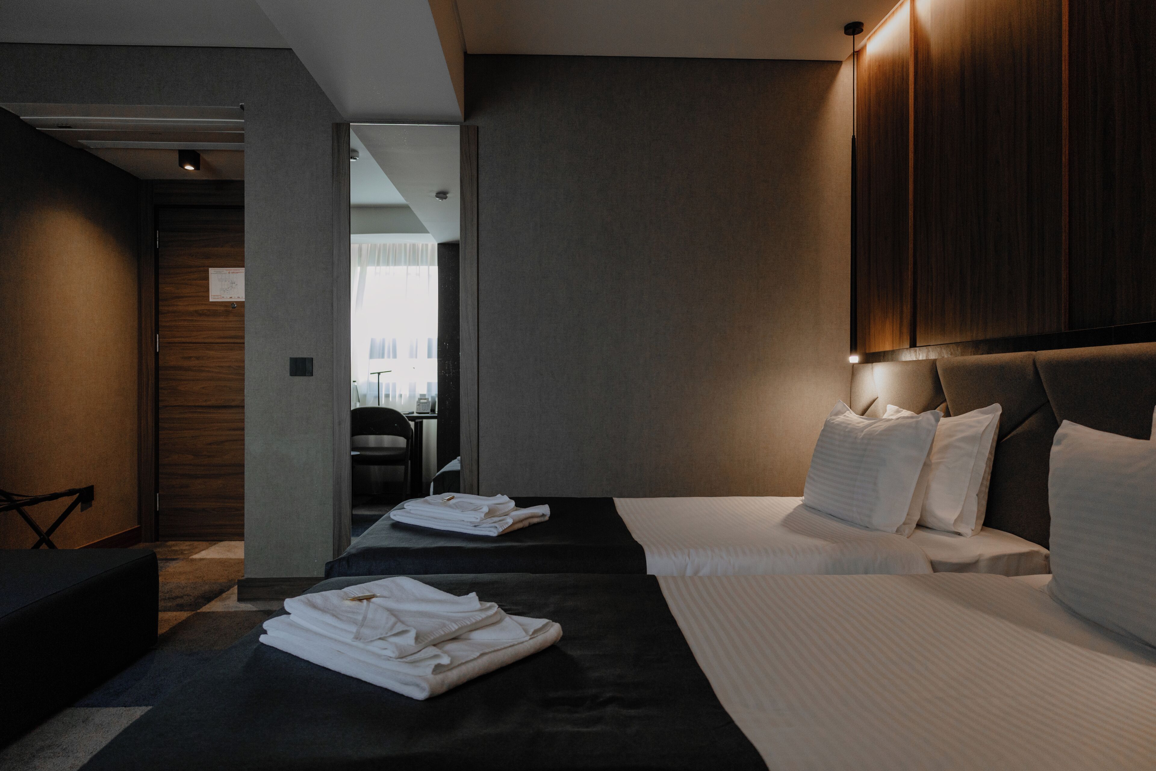 A hotel room with two beds, a sitting area, and a view of the city.