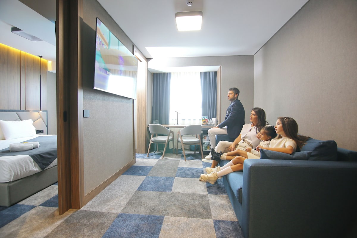 A hotel room with a bed, a sofa, a TV, and a desk with chairs.