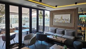 A modern lounge area with a sofa, chairs, and a coffee table. Large windows provide a view of the cityscape. - Lumière Hotel (Belgrade)