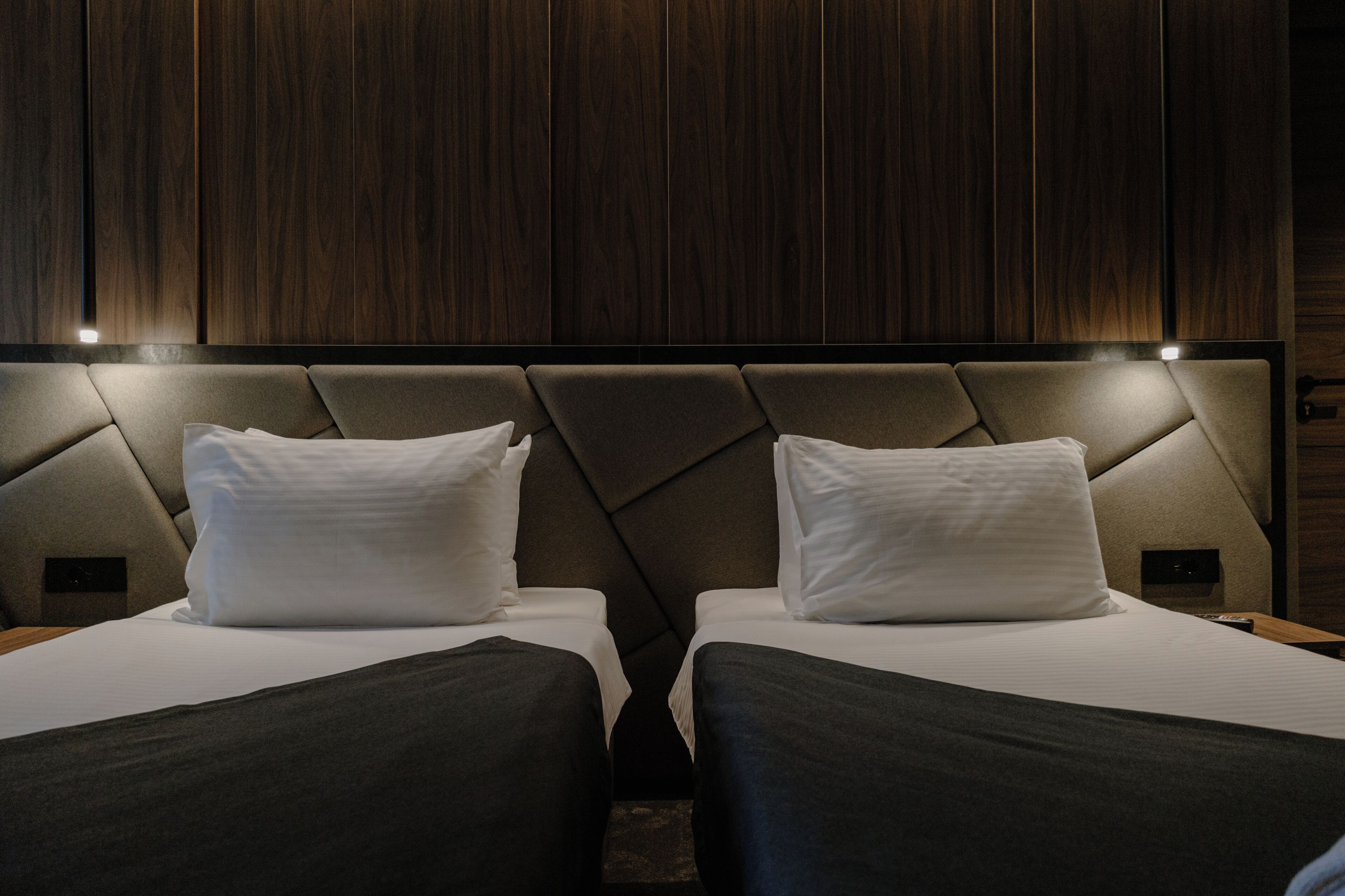A hotel room with two beds, dark wood paneling on the walls, and a modern headboard design.