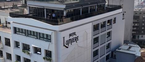 A modern hotel building with a rooftop terrace and a prominent 'Hotel Lumiere' sign.