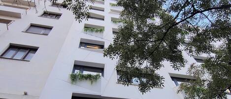 Un hotel llamado HOTEL LUMIERE con una fachada moderna, balcones con vegetación y un cartel llamativo que anuncia Balkan Bet para apuestas en línea.