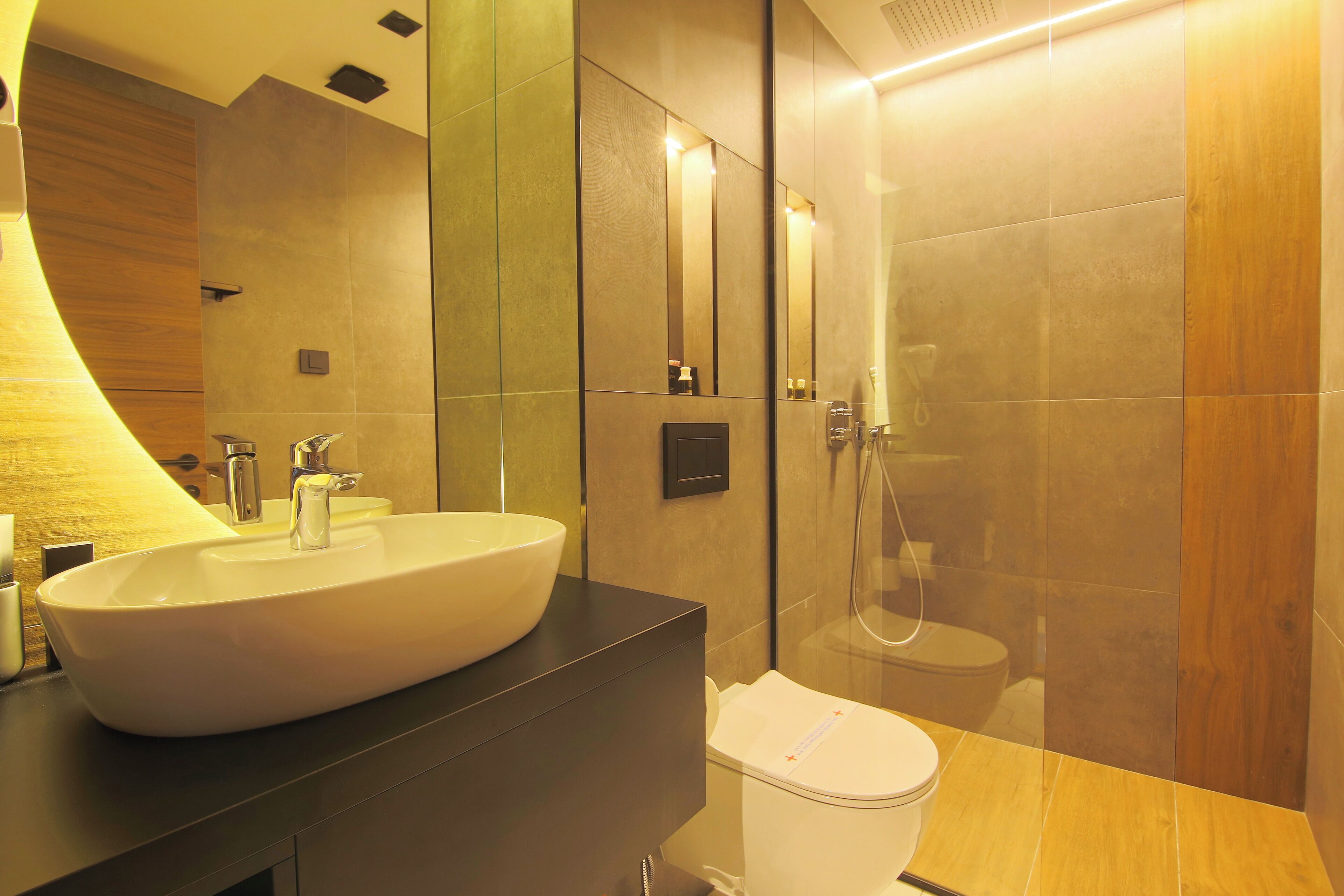 Un baño moderno con un lavamanos grande y blanco, una encimera oscura, un inodoro y una zona de ducha con mampara de vidrio.