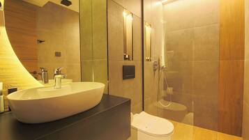 Un baño moderno con un lavamanos grande y blanco, una encimera oscura, un inodoro y una zona de ducha con mampara de vidrio.