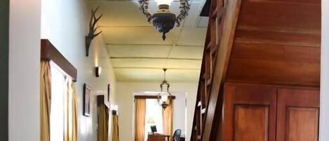 Un couloir en bois orné d’un lustre, d’un grand vase et d’une porte en bois.