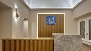 A modern reception desk with a wooden panel and a marble counter, a wall-mounted sign, and a ceiling with recessed lighting. - Heraklean Suites Tropea (Tropea)