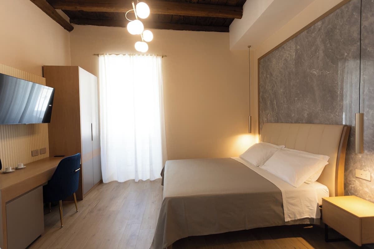 Une chambre à coucher comprenant un lit, une table de chevet, un bureau, une chaise et un téléviseur fixé au mur.