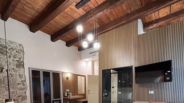 A modern bedroom with a large bed, a wooden ceiling, a stone wall, and a glass door leading to a balcony. - Heraklean Suites Tropea (Tropea)
