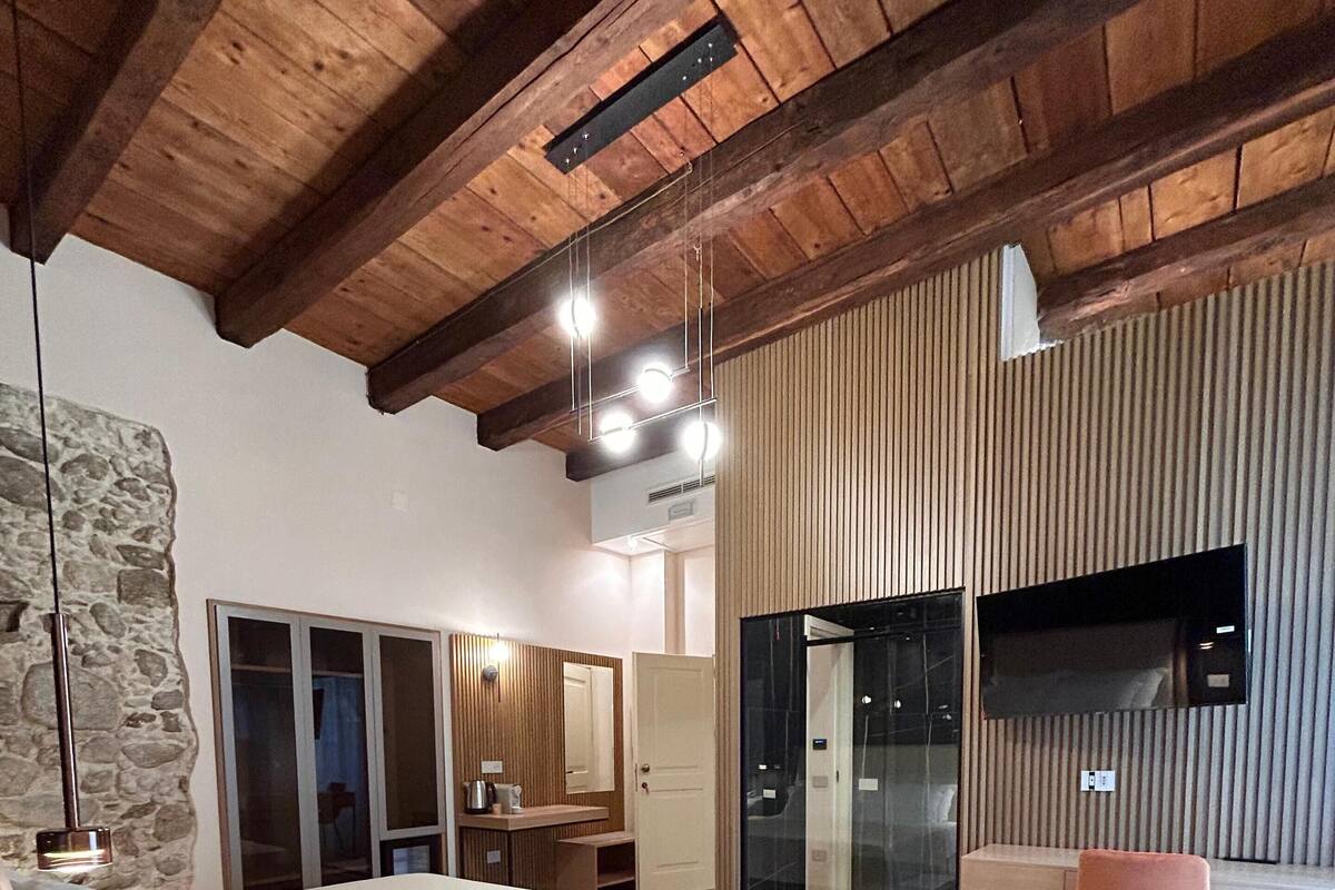 Une chambre à coucher moderne avec un grand lit, un plafond en bois, un mur en pierre et une porte en verre donnant sur un balcon.