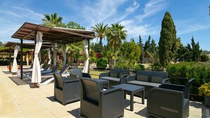 Un patio exterior con mobiliario de mimbre, una pérgola y palmeras.