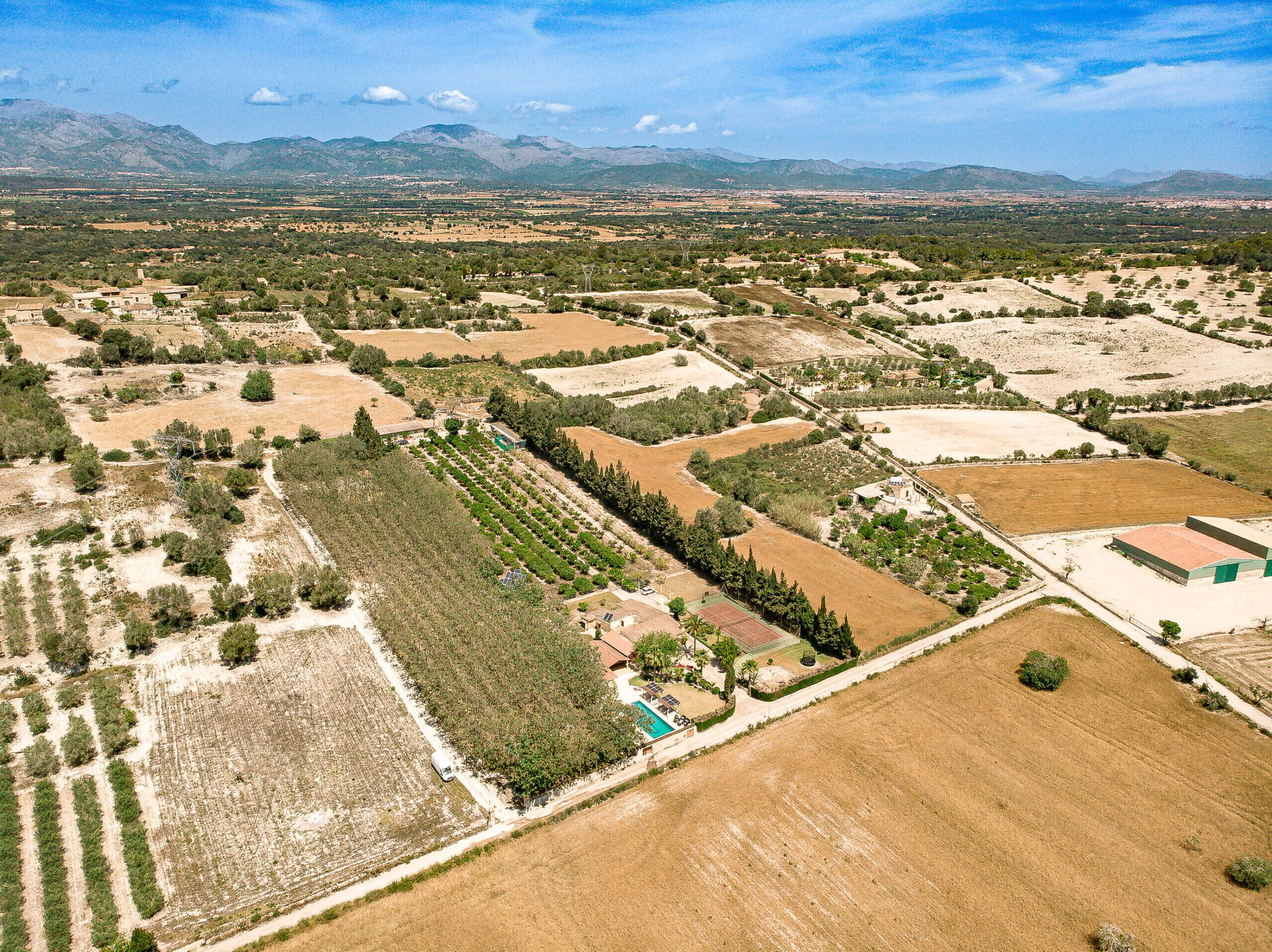 An aerial view of a rural property with fields, a swimming pool, and a small building.