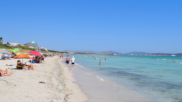 Una playa con gente tomando el sol y nadando, sombrillas y un cielo despejado.