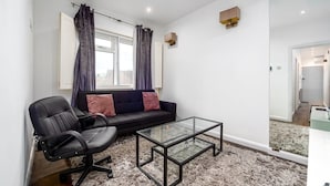 A modern living room with a black leather sofa, a glass coffee table, and a black office chair.