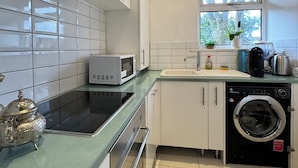 A compact kitchen with white cabinets, a microwave, a stove, a sink, and a washing machine.