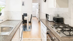 A modern kitchen with a stainless steel sink, a gas stove, a toaster, and a microwave. There is a dining area with a table and chairs visible in the background. - Host Stay Bardsay Road (Liverpool)