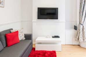 Un soggiorno moderno con un divano grigio, un cuscino rosso, un tavolino da caffè bianco e una TV a schermo piatto montata a parete.