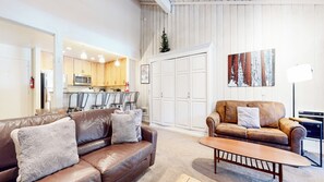 Ein Wohnzimmer mit zwei Sofas, einem Couchtisch, einer Küche im Hintergrund und einem großen, weißen Kleiderschrank.