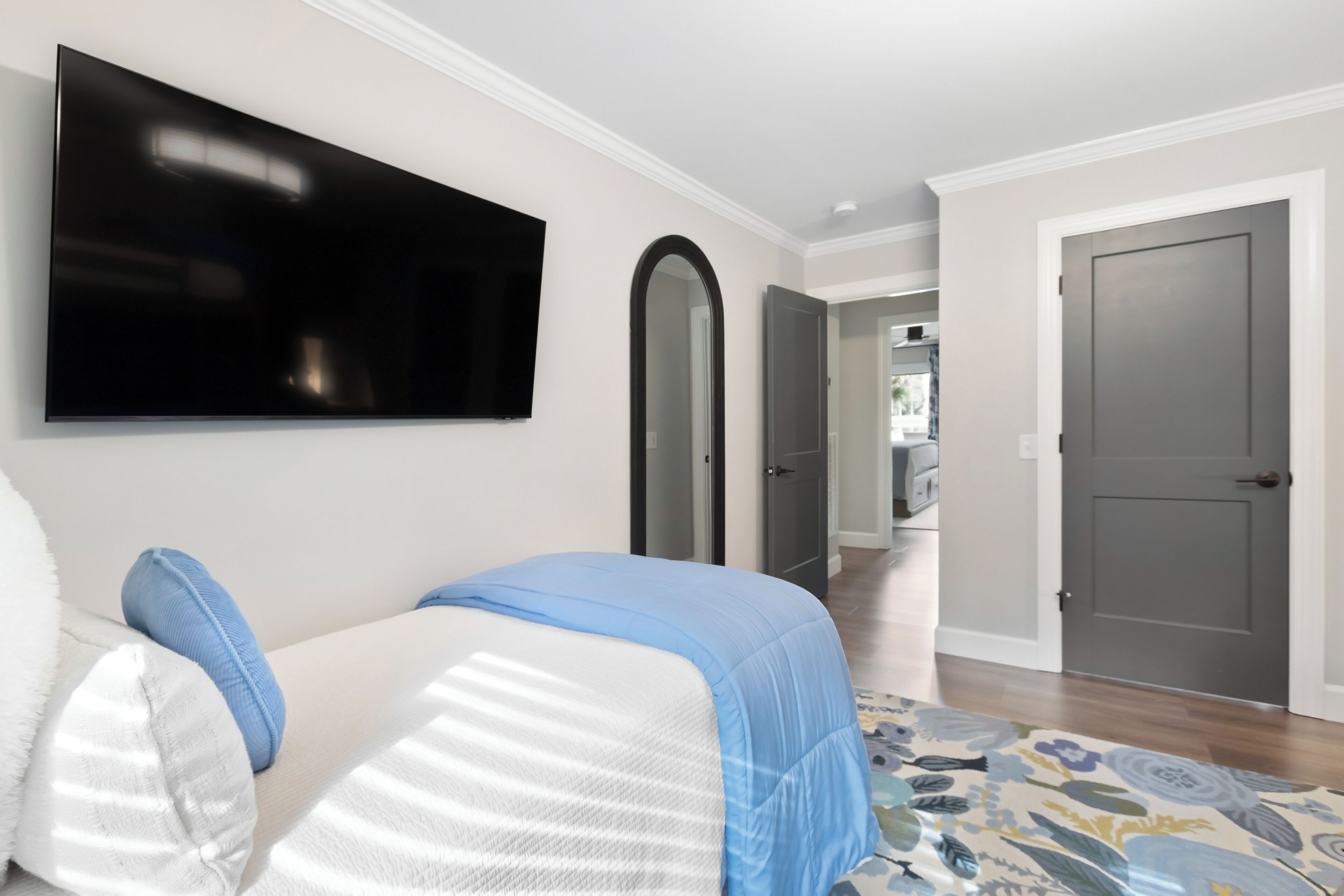 A bedroom with a bed, a TV mounted on the wall, and a door leading to another room.