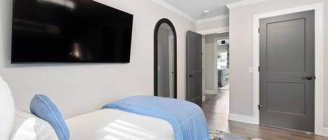 A bedroom with a bed, a TV mounted on the wall, and a door leading to another room.
