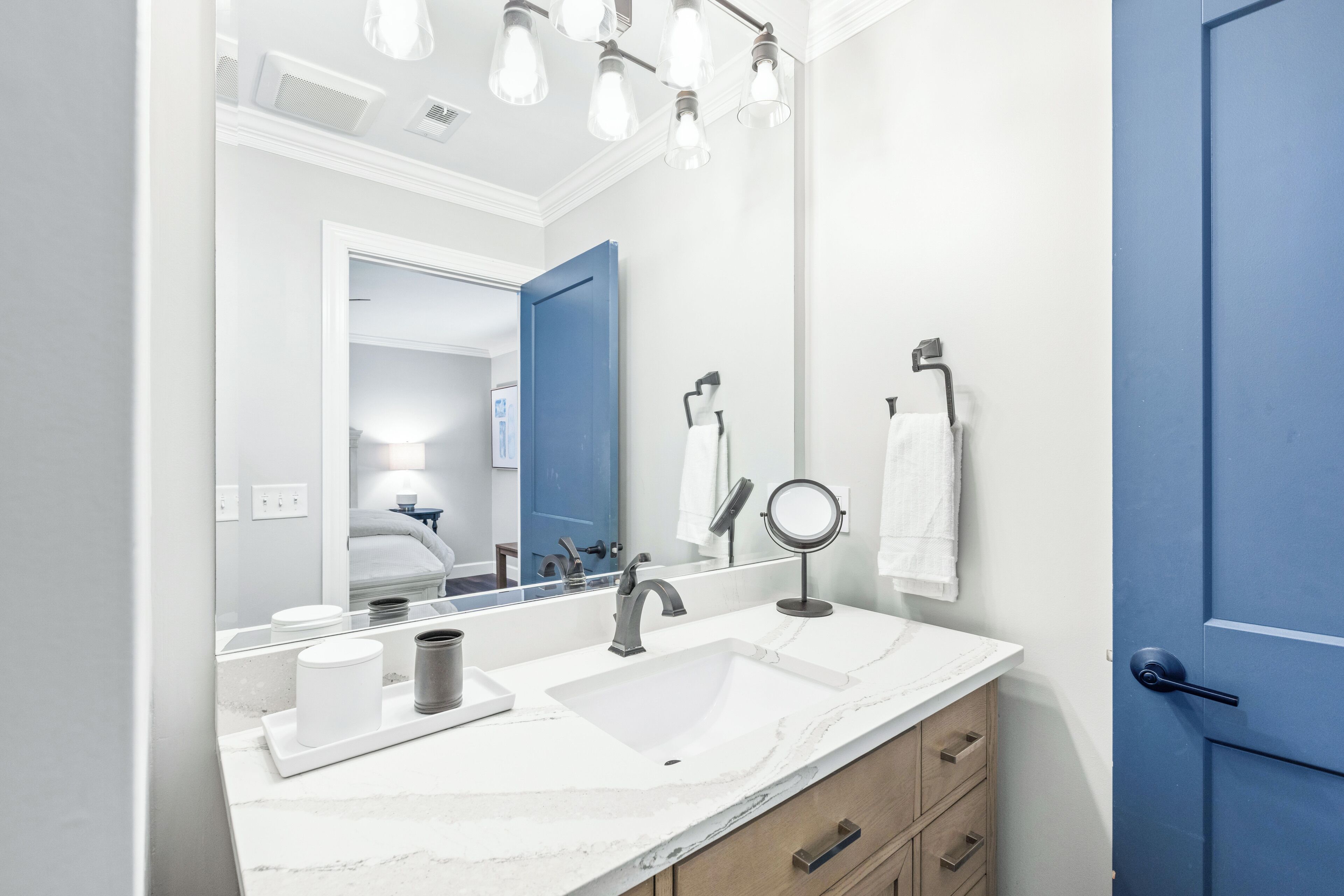 A modern bathroom with a white marble sink, a large mirror, and a blue door.