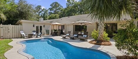 A backyard with a swimming pool, lounge chairs, and a covered patio area.