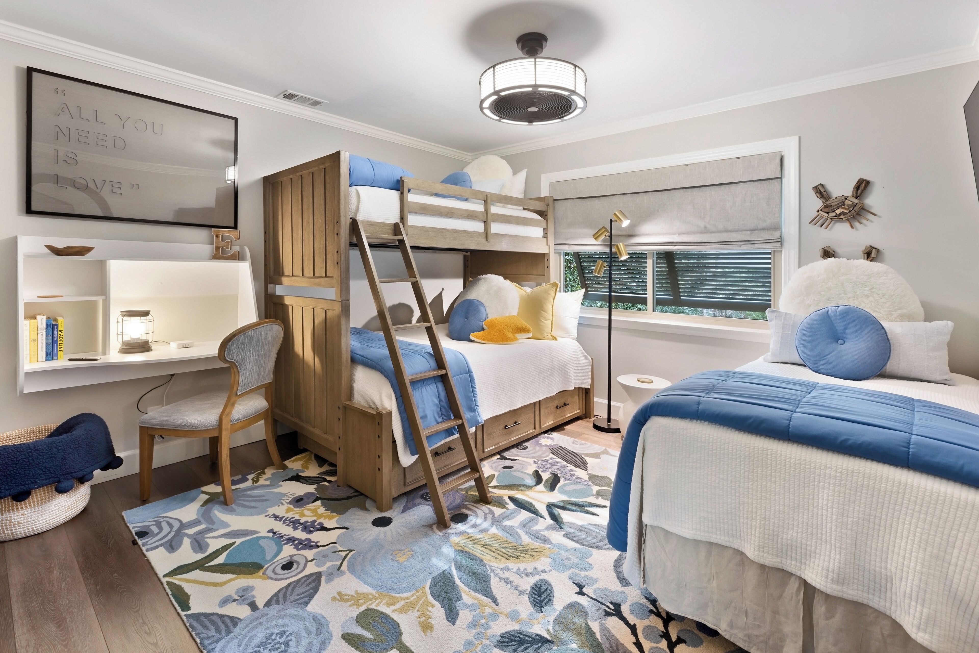 A bunk bed room with a ladder, a desk, a chair, and a window with blinds.