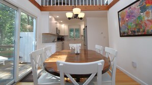 Un coin repas avec une table en bois et des chaises blanches, un lustre et un tableau coloré accroché au mur.