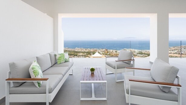 A modern living room with a sofa, two armchairs, a coffee table, and a view of the sea.