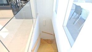 Un interior moderno con escalera de madera, barandales de vidrio y vistas a un área de estar exterior.