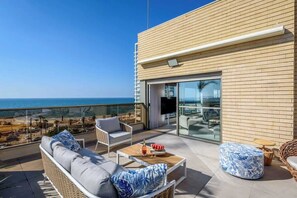A balcony with wicker furniture, a glass door leading to an indoor area, and a view of the beach. - #Breathtaking 4BR/3BA Duplex Seafront (Tel Aviv-Yafo)