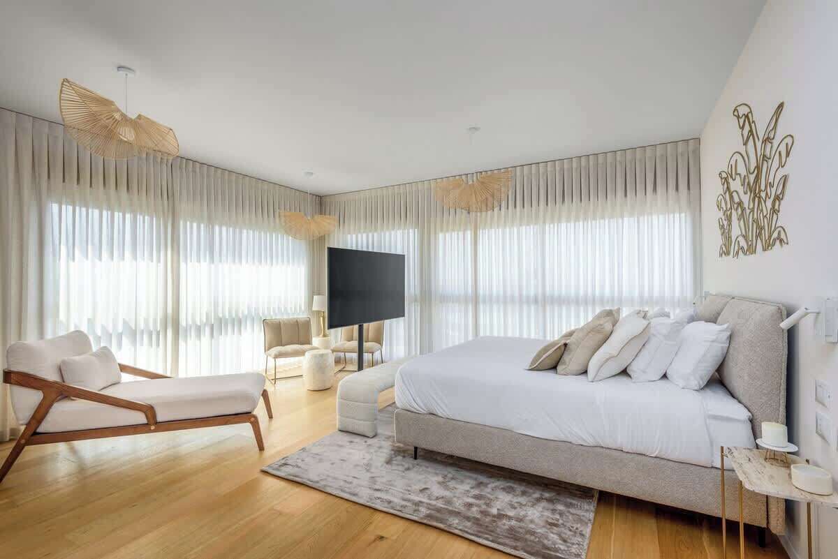 A modern bedroom with a large bed, a sofa, a TV, and a decorative wall piece.