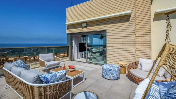 Un balcón con mobiliario de mimbre, una puerta de cristal y vista al océano.