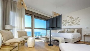 Una habitación de hotel con un ventanal grande, una cama, un sofá, un sillón y un televisor.