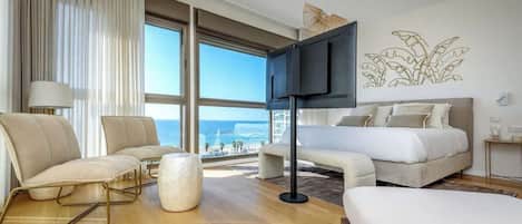 A hotel room with a large window, a bed, a sofa, a chair, and a TV.