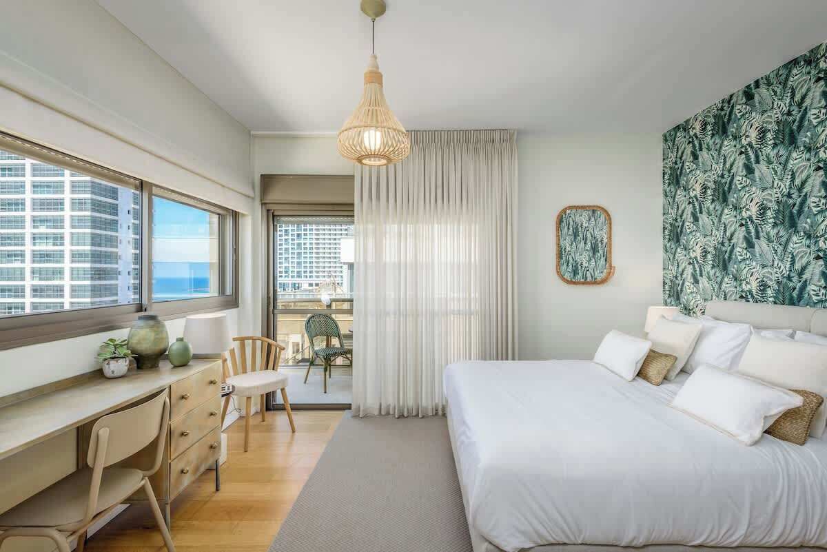 Ein Hotelzimmer mit Bett, Schreibtisch, Stühlen und Blick auf Gebäude, mit Vorhang.