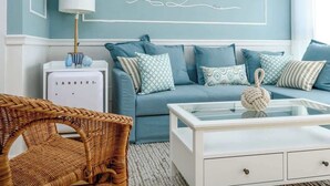 A living room with a blue sofa set, a white coffee table, a wicker chair, and a wall-mounted lamp. - #Breathtaking 4BR/3BA Duplex Seafront (Tel Aviv-Yafo)