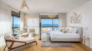 A modern bedroom with a large bed, a seating area with a chaise lounge, and a view of the beach through large windows. - #Breathtaking 4BR/3BA Duplex Seafront (Tel Aviv-Yafo)