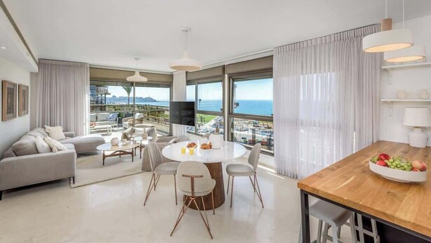 A modern living room with a round dining table, comfortable seating, and large windows offering a view of the sea. - #Breathtaking 4BR/3BA Duplex Seafront (Tel Aviv-Yafo)
