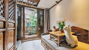 A traditional room with a wooden sofa, a table with a vase of flowers, and a view through a wooden lattice door.