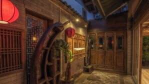 A traditional courtyard with wooden doors, a large wooden water wheel, and red lanterns.