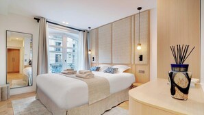 Een moderne hotelkamer met een groot bed, een houten hoofdbord, een nachtkastje, een spiegel en uitzicht op de stad door het raam.