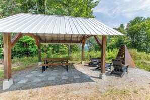 A wooden pavilion with a corrugated metal roof, a picnic table, and two lounge chairs.