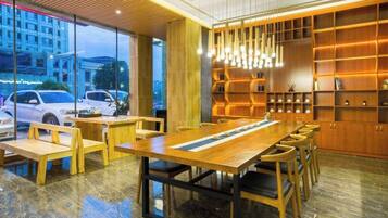A modern interior with a long wooden table and chairs, a glass wall with a view of the street, and shelves with books and decorative items.
