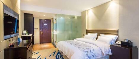 Una habitación de hotel moderna con una cama grande, televisión, escritorio y cabina de ducha de vidrio.