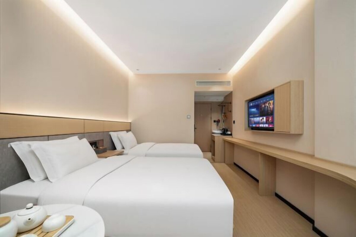 A modern hotel room with a large bed, bedside tables, a TV, and a small kitchenette area.
