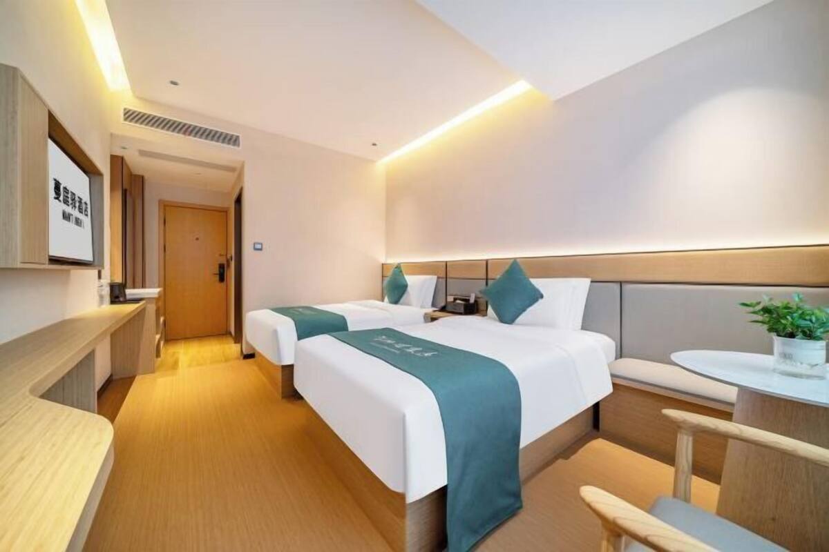 A hotel room with two beds, a bedside table, a small seating area, and a plant.